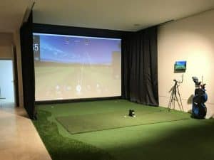 best projector for golf simulator, A golfer swings their club at a golf ball on a driving range